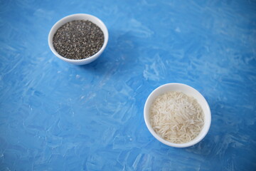 Rice and chia seeds are organic food for a healthy diet. In a round bowl. Two white cups. The blue background is painted with oil paints.