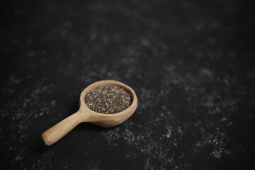 Spices. Chia seeds in a wooden spoon on a black and gray background. Blurred background