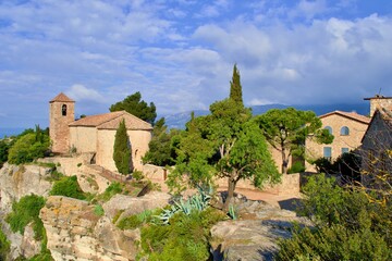 Fototapeta na wymiar Village with romanesque church of Santa Maria de Siurana on top of rock, view into valley, mountains on the background. Blue sky with white clouds. Siurana, Catalonia, Spain.