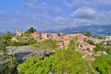 Village with romanesque church of Santa Maria de Siurana on top of rock, view into valley, mountains on the background. Blue sky with white clouds.  Siurana, Catalonia, Spain.