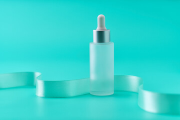 Natural cosmetics, serum for hair and skin care and mint ribbon on a blue background, copy space for your text.
