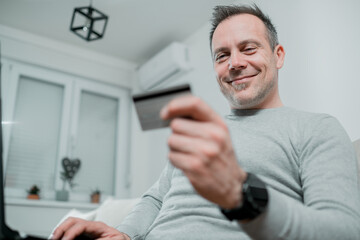 man wearing grey sweater smiling and holding a credit card