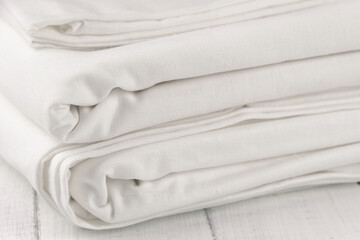 Stack of clean bed linen on white wooden table. Structure of fabric on bends
