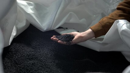A man pours black polymer granules from his hands in a garbage recycling plant