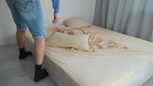 Man makes up his bed in the morning in the bedroom. He carefully spreads the duvet cover on the bed. Household chores, daily routine in the morning. Man makes his bed by himself.