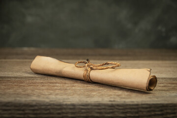 Parchment scroll with burnt edges is tied with rope. On old wooden table, mysterious document, invitation to event - 428437765