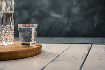 Glass of vodka on wooden plank table. Transparent decanter of beverage. Atmosphere bar drinking. Copy space for text on dark wall. Concept solitary alcoholism - obrazy, fototapety, plakaty