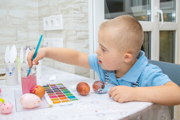 A boy with Down syndrome draws, a genetically ill child paints Easter eggs, preparation for Easter,...