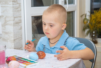 A boy with Down syndrome draws, a genetically ill child paints Easter eggs, preparation for Easter,...