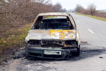 Plakat Burned car after an accident on the asphalt road. Front view. Arson of a car, criminal showdowns