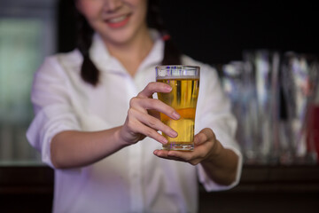 Beautiful Asian woman holding a glass of beer close up on background inside bar.