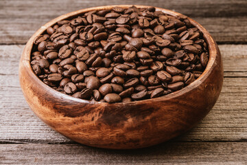 Roasted coffee beans in bowl. Texture of wooden table. Presentation of drink sort, freshness and naturalness