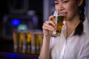 Beautiful Asian woman holding a glass of beer close up on background inside bar.