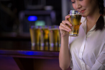 Beautiful Asian woman holding a glass of beer close up on background inside bar.