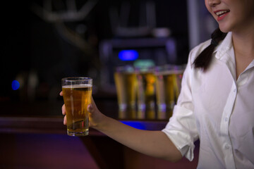 Beautiful Asian woman holding a glass of beer close up on background inside bar.