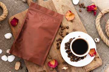 Blank coffee packaging on a wooden board, coffee seeds, cup with coffee, dry rose petals on a jute background, coffee packaging mockup with empty space to display your branding design.