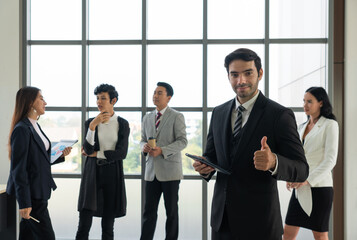 portrait of young caucasian confident businessman with smiling face stnading in office with background of multiethnic colleagues. diversity in business concept