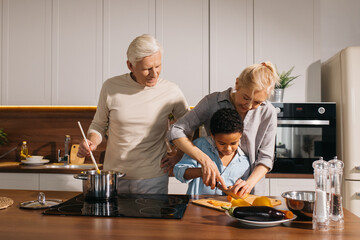 Mother teaching her little son holding knife and cut fresh vegetables in kitchen