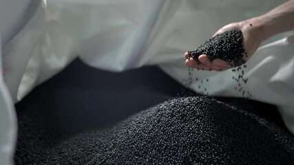 A man pours black polymer granules from his hands in a garbage recycling plant
