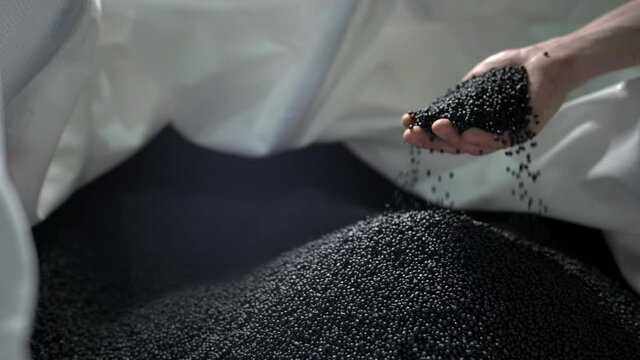 A man pours black polymer granules from his hands in a garbage recycling plant