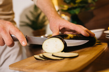 Man chopping eggplant on wooden chopping board in modern kitchen