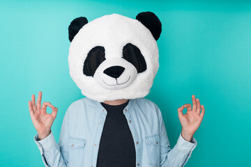 Young man wearing panda mask over isolated aquamarine studio background in zen pose