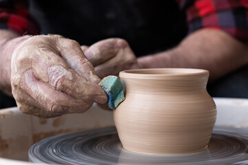 Fototapeta na wymiar Male hands cleaning with sponge pottery on a potter wheel.