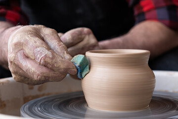 Male hands cleaning with sponge pottery on a potter wheel.