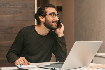 Work from home. A man at home talking on the phone. A young man sitting at a laptop