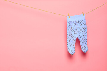 Baby clothes on a clothesline on pink background .