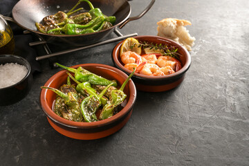 Spanish tapas, fried pimientos or padron peppers and shrimps in traditional bowls on a dark gray...