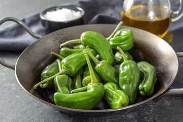 Fresh green pimientos or peppers de padron in an iron pan. Fried in olive oil, and sprinkled with sea salt is a typical tapa meal in Spain. Dark gray slate background, selected focus