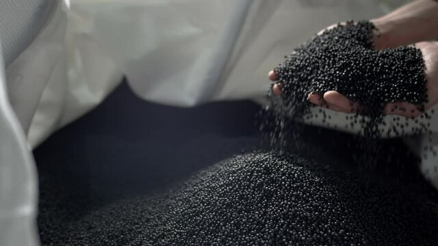 A man pours black polymer granules from his hands in a garbage recycling plant