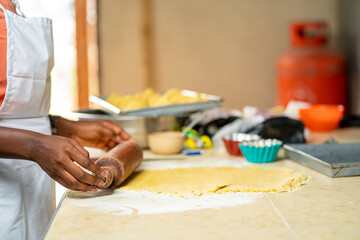 landscape view of black hand and a wooden rolling pin, pressing on a mixed flour with other materials blurred at the background- baking concept