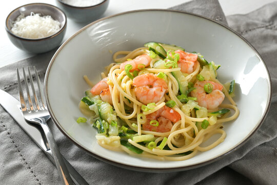 Pasta dish from spaghetti, zucchini, spring onions and prawns in a grey plate on a napkin with parmesan bowl and cutlery, Mediterranean cooking