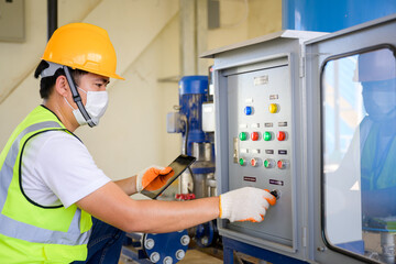 Young electrical engineer wearing a mask Inspect the electrical control cabinet and electrical control system in the building and perform daily checks by a service room technician at the factory
