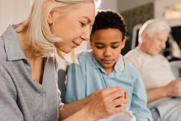 Senior woman showing a needle to her grandson while doing needlework at home