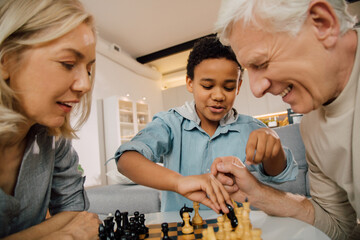 Father, mother and their multiracial son sitting at the table and playing chess