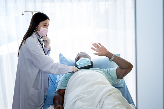 Blurred soft images of African American man patient wearing a surgical mask Lying on the patient's bed And the woman doctor examining the condition From viral infection, to health care concept