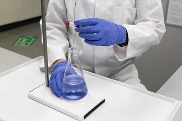 Chemist with gloved hands and a white labcoat in a laboratory analysing a sample by titration 