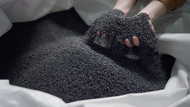 Hands lift polymer granules from a bag in a garbage recycling plant.