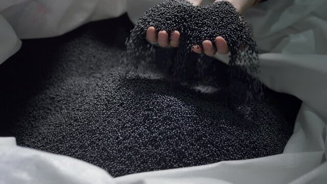 Hands lift polymer granules from a bag in a garbage recycling plant.