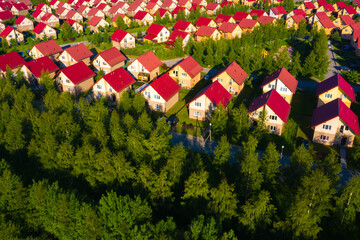 Houses of same type as a symbol of suburbia. Houses with a red roof view from a quadcopter. Identical cottages on a summer day. Concept of living in modern suburbia. Suburb surrounded by conifers