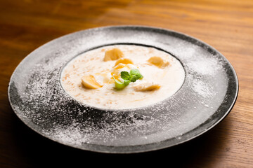 Photo of beautiful plate with oatmeal and banana decorated with mint over wooden table in restaurant