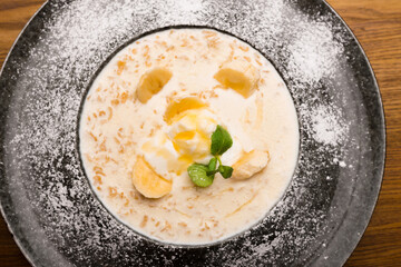 Close up photo of beautiful plate with oatmeal and banana decorated with mint over wooden table in restaurant