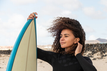 Multiracial pretty surfer girl portrait standing on the beach holding her surfboard