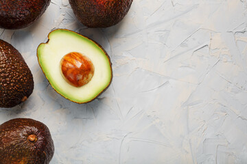 Avocado halves with whole Hass fruits on a background of gray concrete, stone or slate.