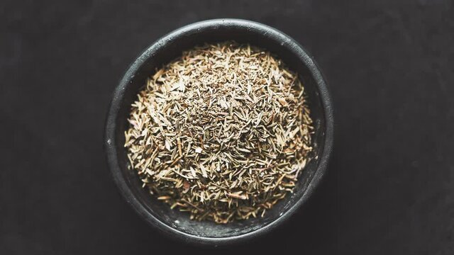 Dried thyme in wooden bowl placed on black table