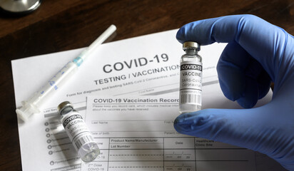 Coronavirus vaccine vial in doctor`s hand on medical forms background