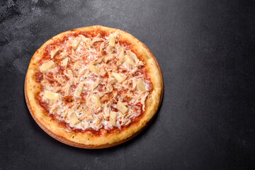 Tasty fresh oven pizza with tomatoes, cheese and pineapple on a dark concrete background